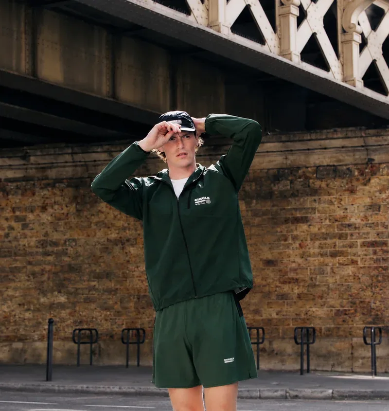 Homme portant une veste de running verte et un short assorti de la collection Circle x Octobre Éditions, sous un pont à Paris.