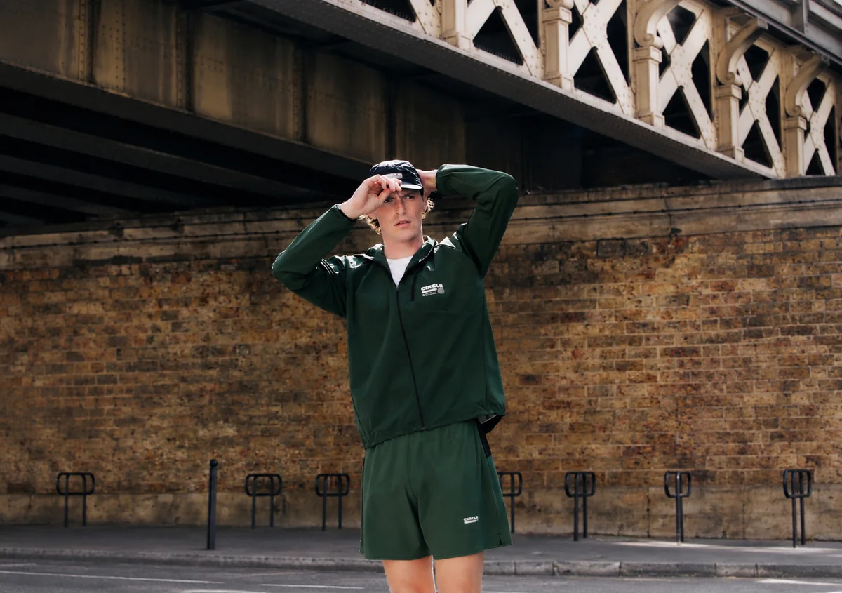 Homme portant une veste de running verte et un short assorti de la collection Circle x Octobre Éditions, sous un pont à Paris.
